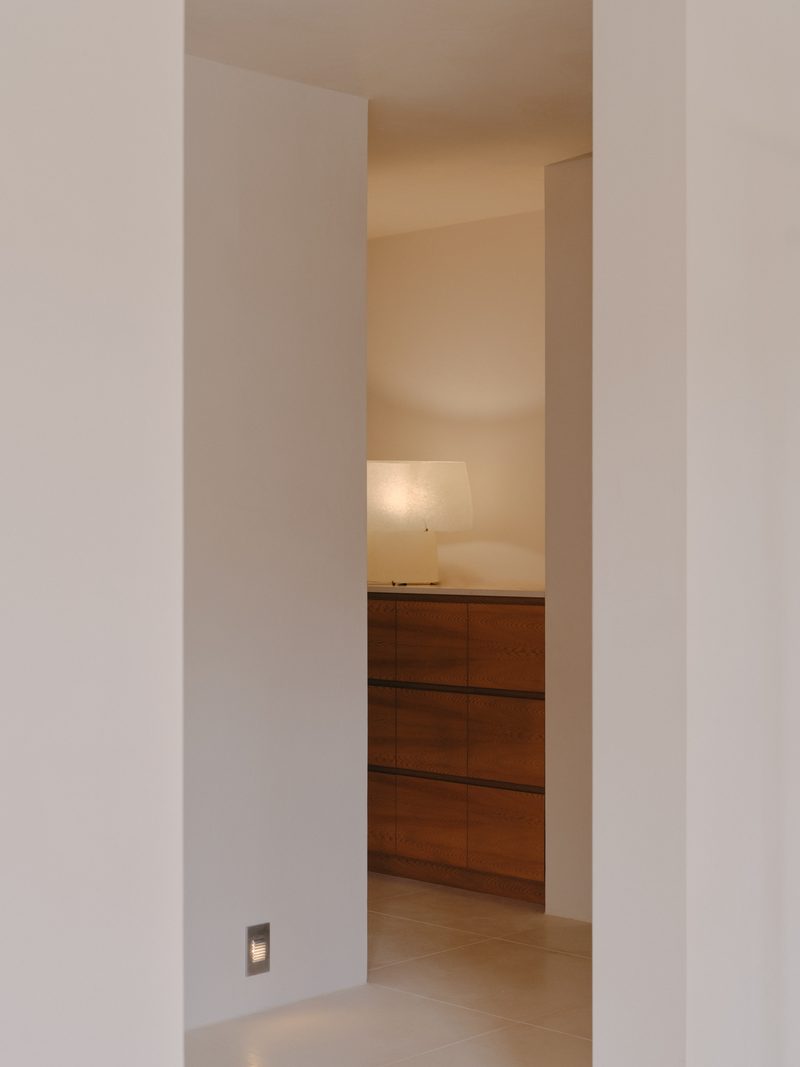 Doorway framing a timber cabinet and lamp in a white interior